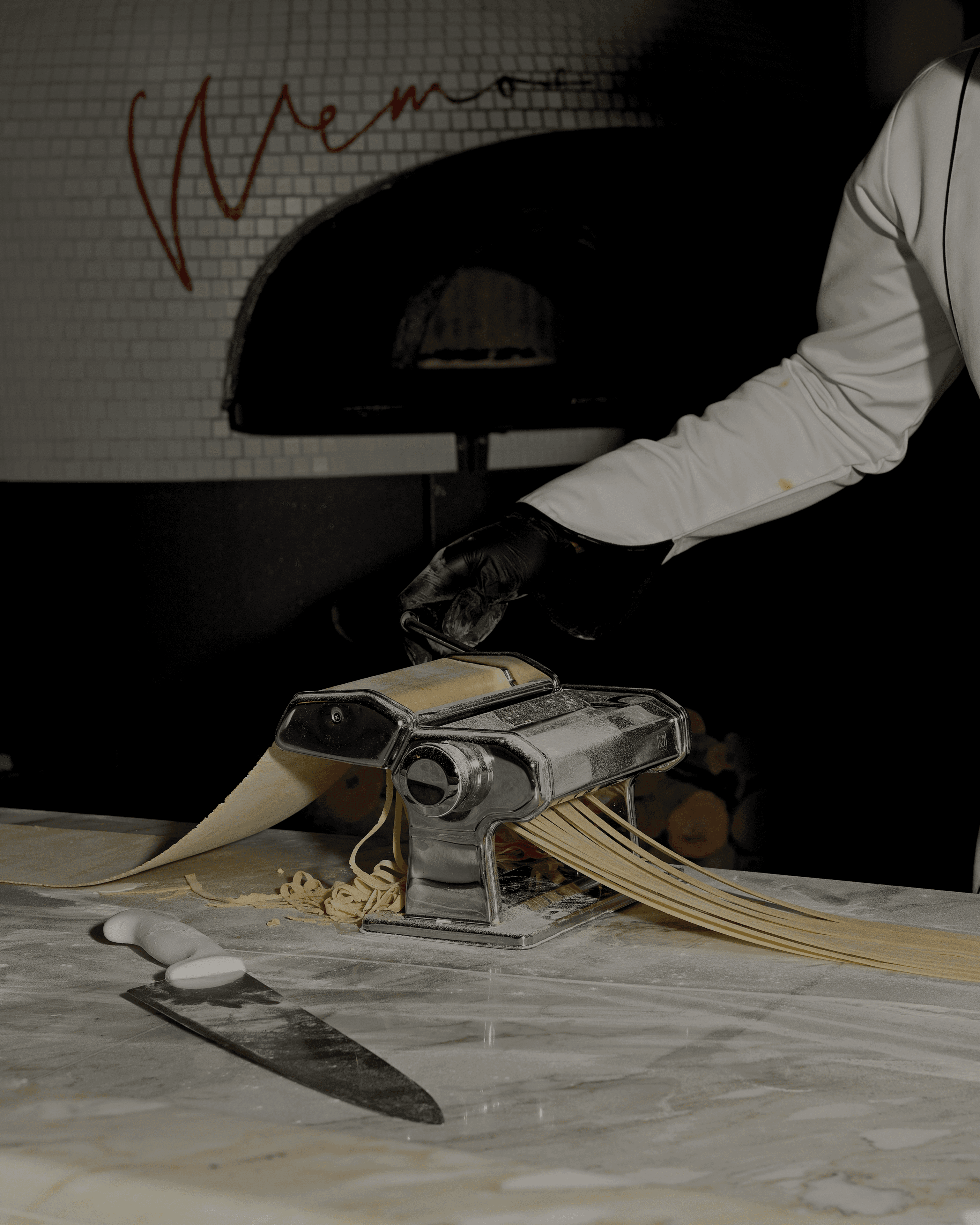 MEMOS chef rolling fresh pasta sheets through a pasta machine in front of the wood-fired oven